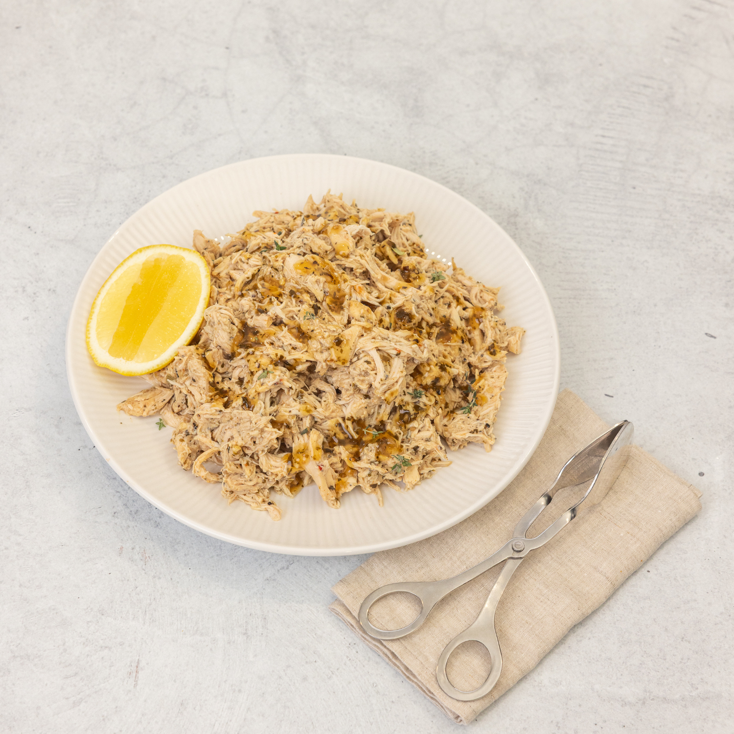 Plated dish of shredded chicken salad with a lemon wedge on a light gray surface.
